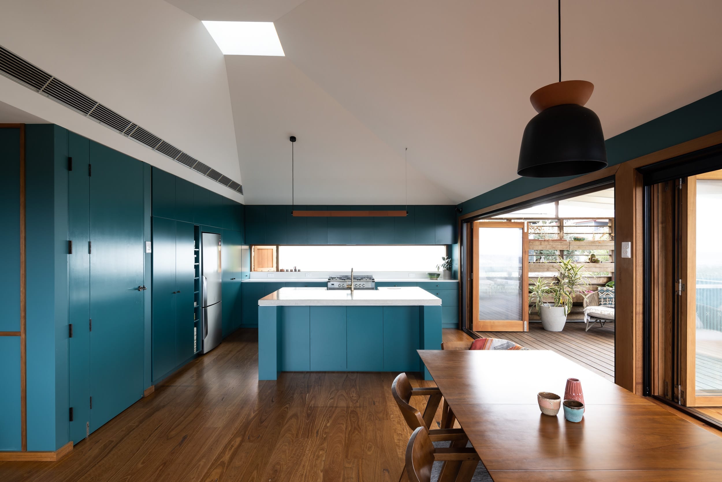 A stunning blue kitchen, with open bifold timber doors leading onto a deck