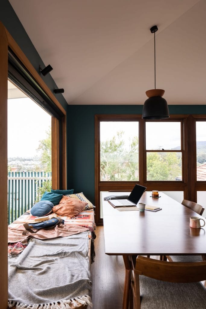 A multipurpose dining table with bench seat covered in blankets and cushions, laptop on table