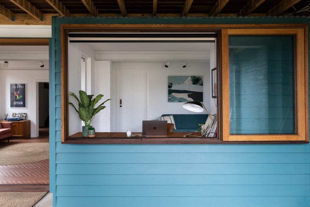 Face sliding timber window open into a study against a deep blue timber exterior