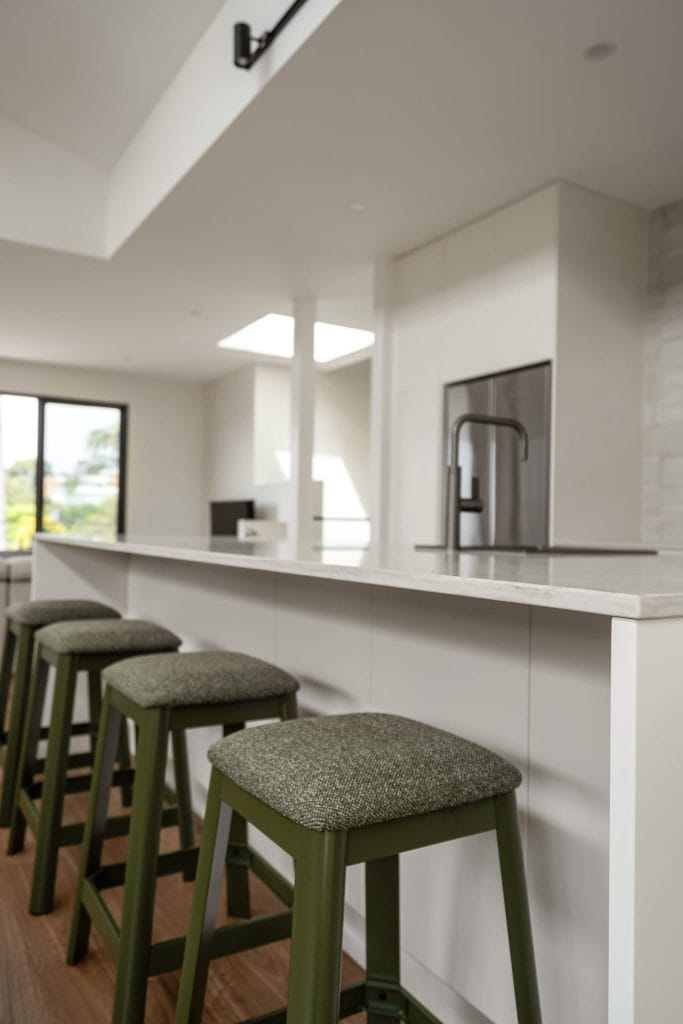 Detail of olive green bar stools with padded top in a white kitchen