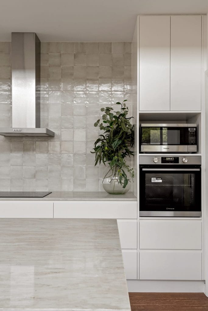 A minimalist white and grey kitchen with built in oven and microwave