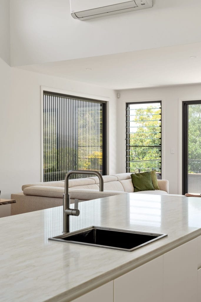 A modern kitchen and living room with louvre windows to capture coastal breezes by YourBuild Construct