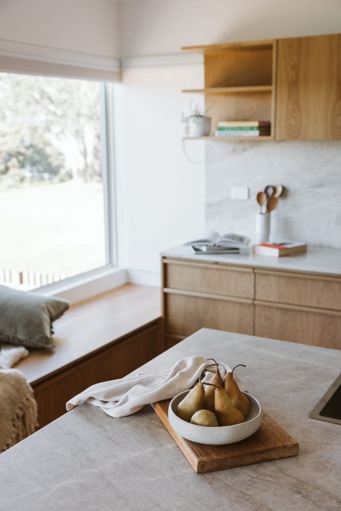 Detail of pears in a bowl on a kitchen benchtop with timber cabinetry behind.